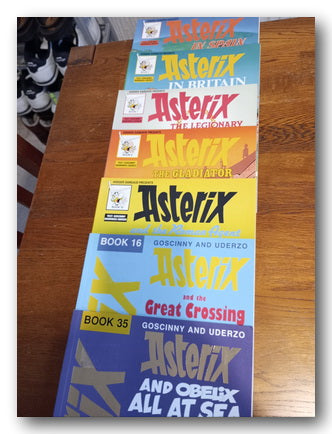 Collection of Asterix comic book covers arranged vertically on a wooden surface.