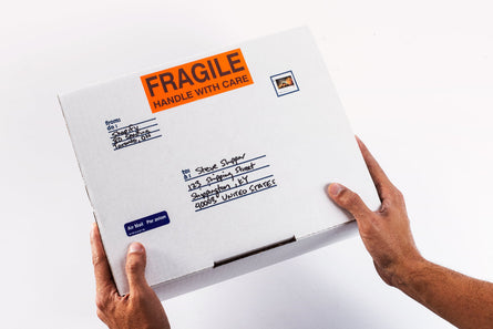 A small white package with Fragile, Handle with care on it.